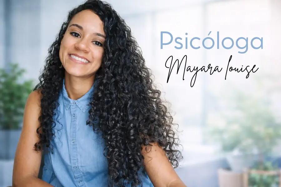 Psicóloga sorridente com cabelos longos e cacheados, usando blusa azul, em ambiente claro e acolhedor, transmitindo confiança, empatia e bem-estar